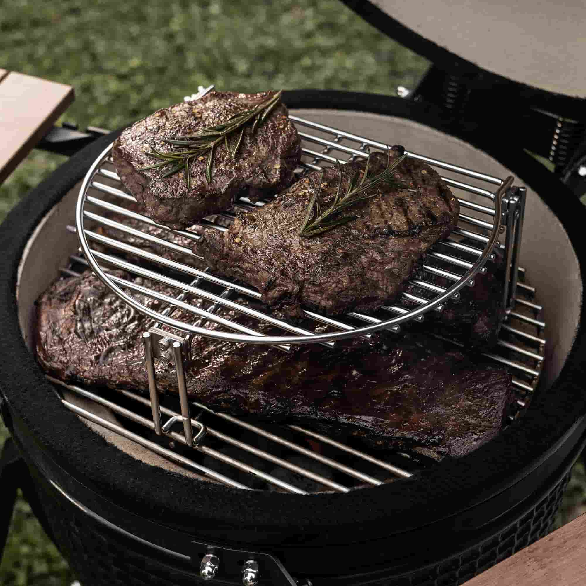 Viande grillée avec branches de romarin sur une grille inox à deux niveaux dans un barbecue kamado ouvert.