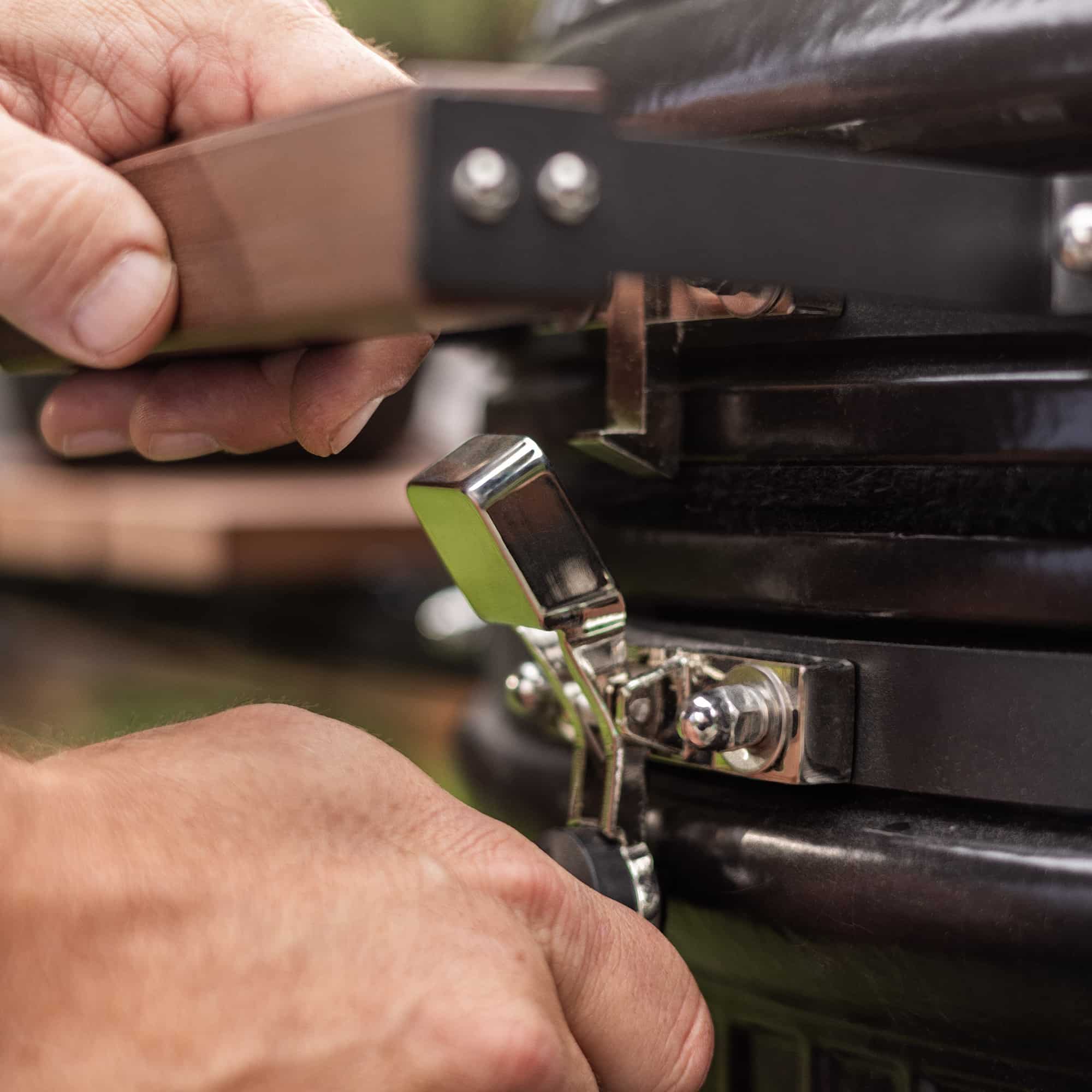 Main fermant la charnière métallique d’un barbecue kamado avec poignée en bois.