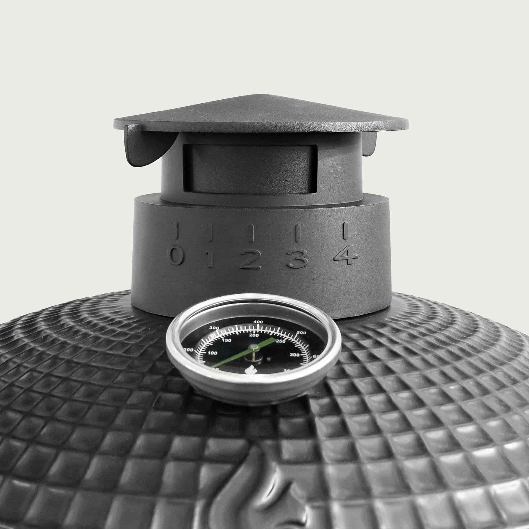 Gros plan sur la cheminée en fonte émaillée d’un barbecue Kamado, avec graduations de réglage de l’air et thermomètre intégré pour un contrôle précis de la température.