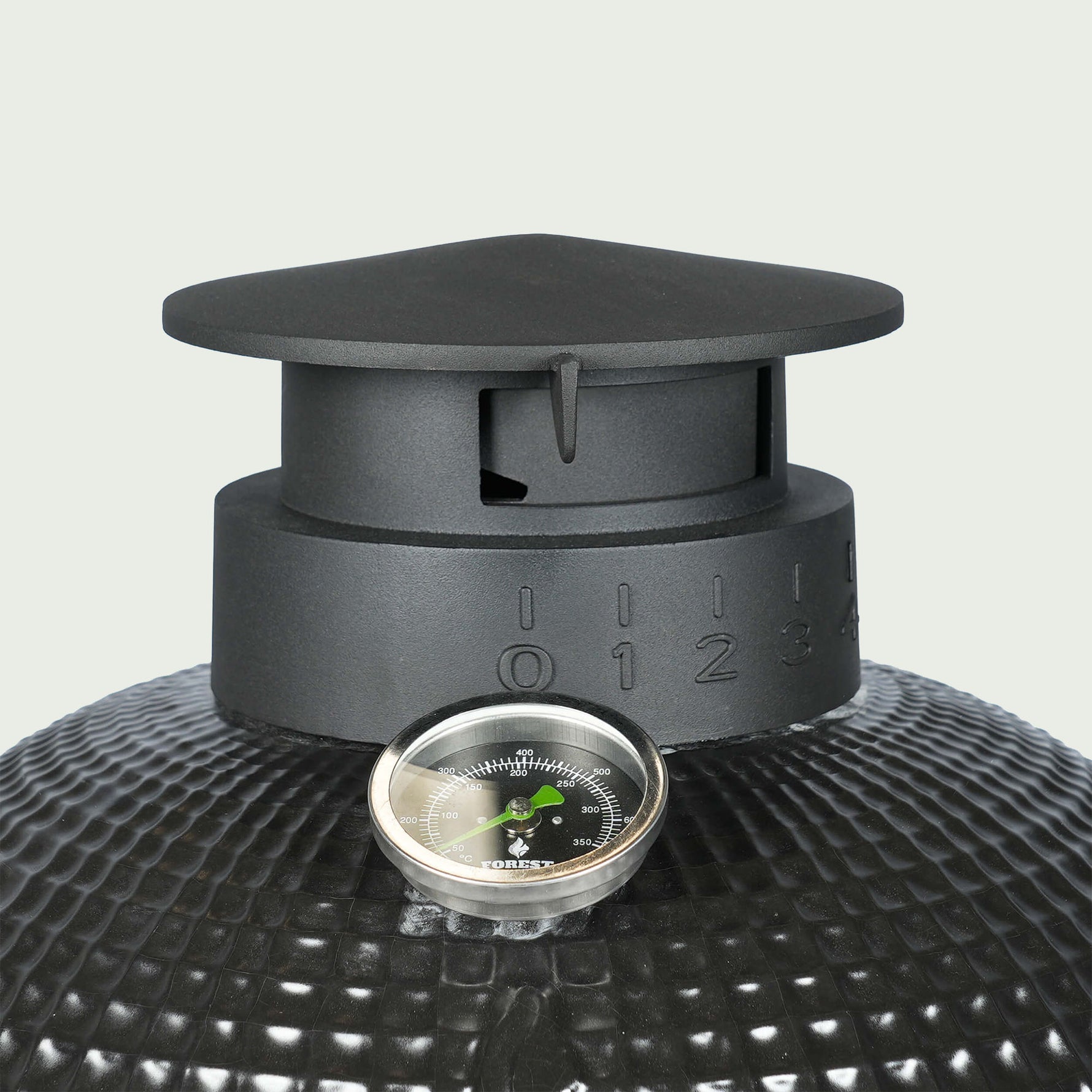 Gros plan sur la cheminée en fonte émaillée d’un barbecue Kamado, avec graduations de réglage de l’air et thermomètre intégré pour un contrôle précis de la température.