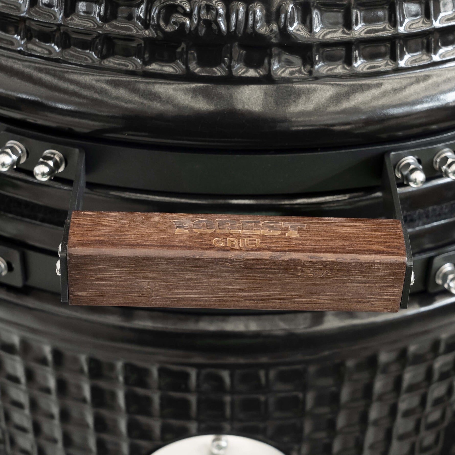Poignée en bois gravée Forest Grill, alliant élégance naturelle et confort d’utilisation sur la céramique texturée du barbecue.