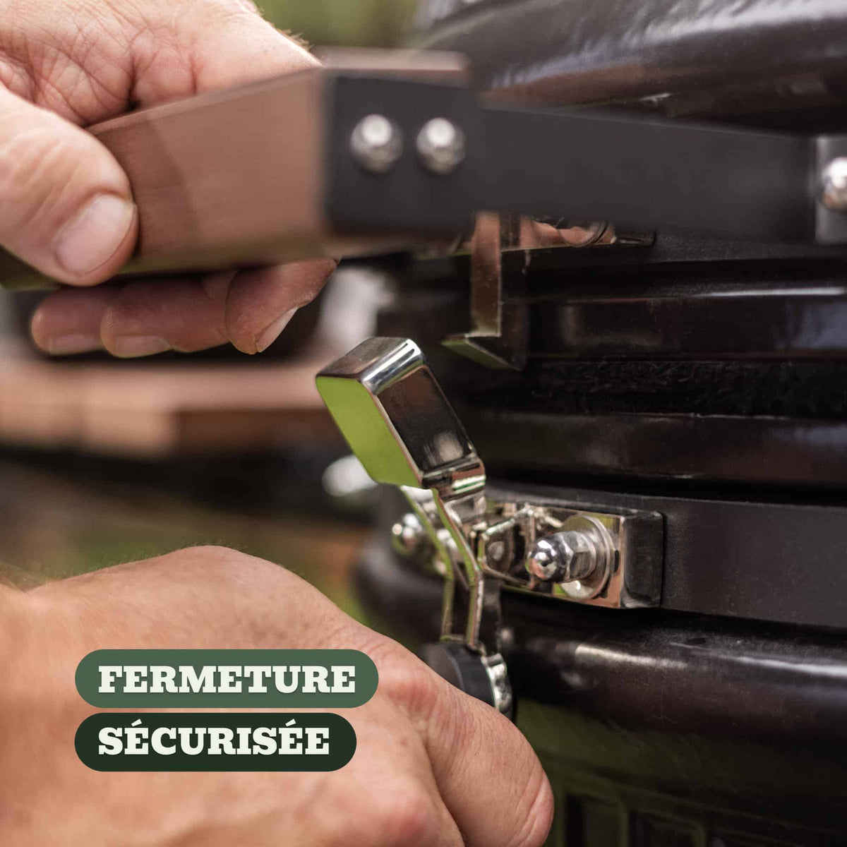 Gros plan sur la fermeture sécurisée d’un barbecue Kamado, montrant une main actionnant un loquet métallique robuste pour maintenir le couvercle bien scellé.