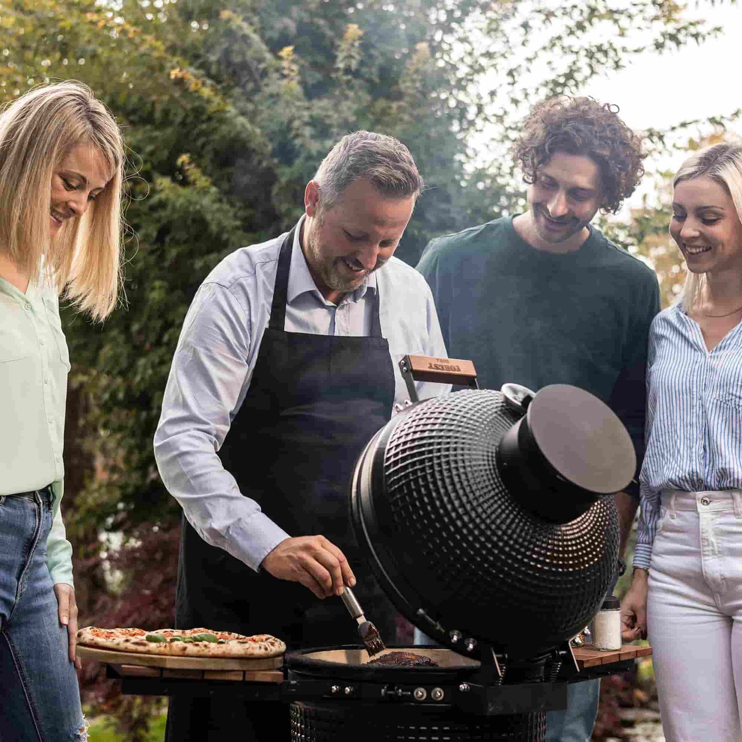 Groupe de personnes profitant d’un moment convivial autour d’un barbecue Kamado Forest Grill dans un jardin.