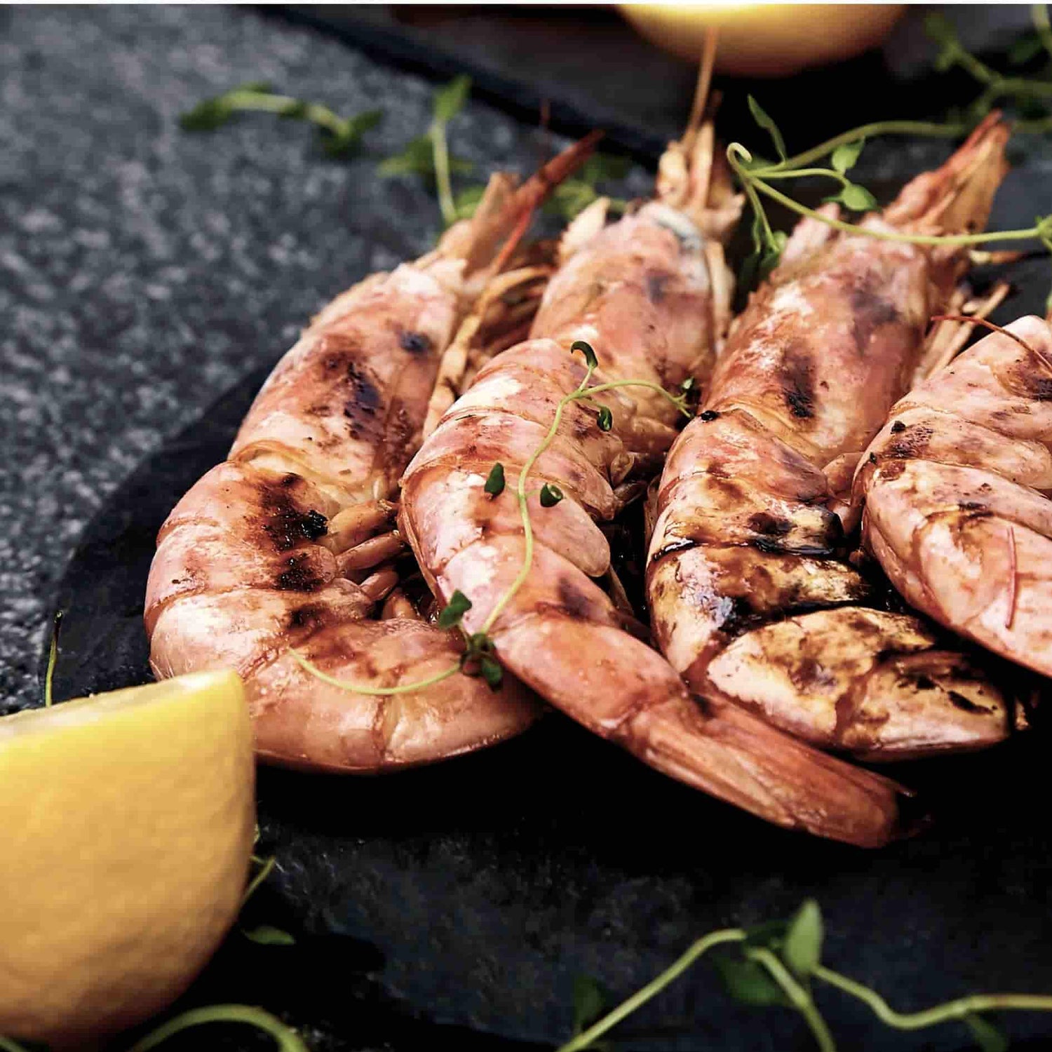 Gambas grillées et flambées au whisky sur barbecue Kamado Forest Grill, servies avec herbes fraîches et quartier de citron.