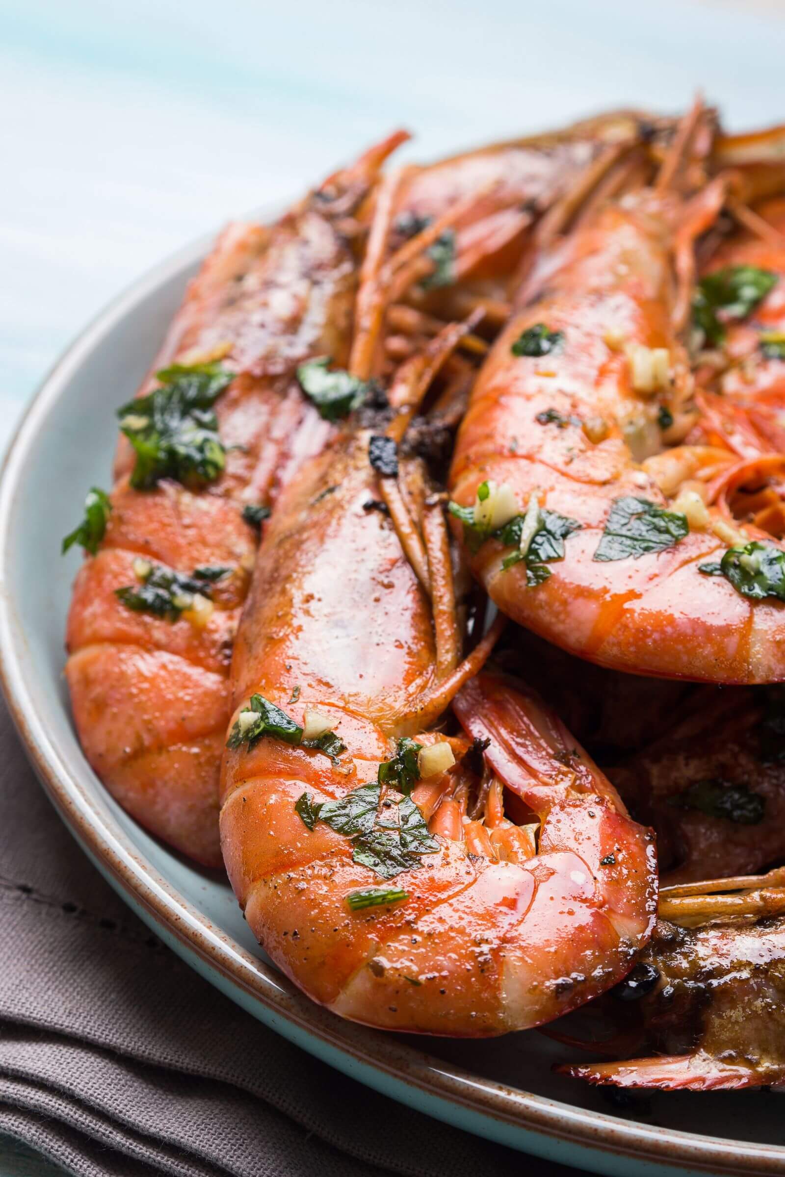 Gambas grillées à la plancha avec une marinade à l’ail et au persil, servies dans une assiette creuse.