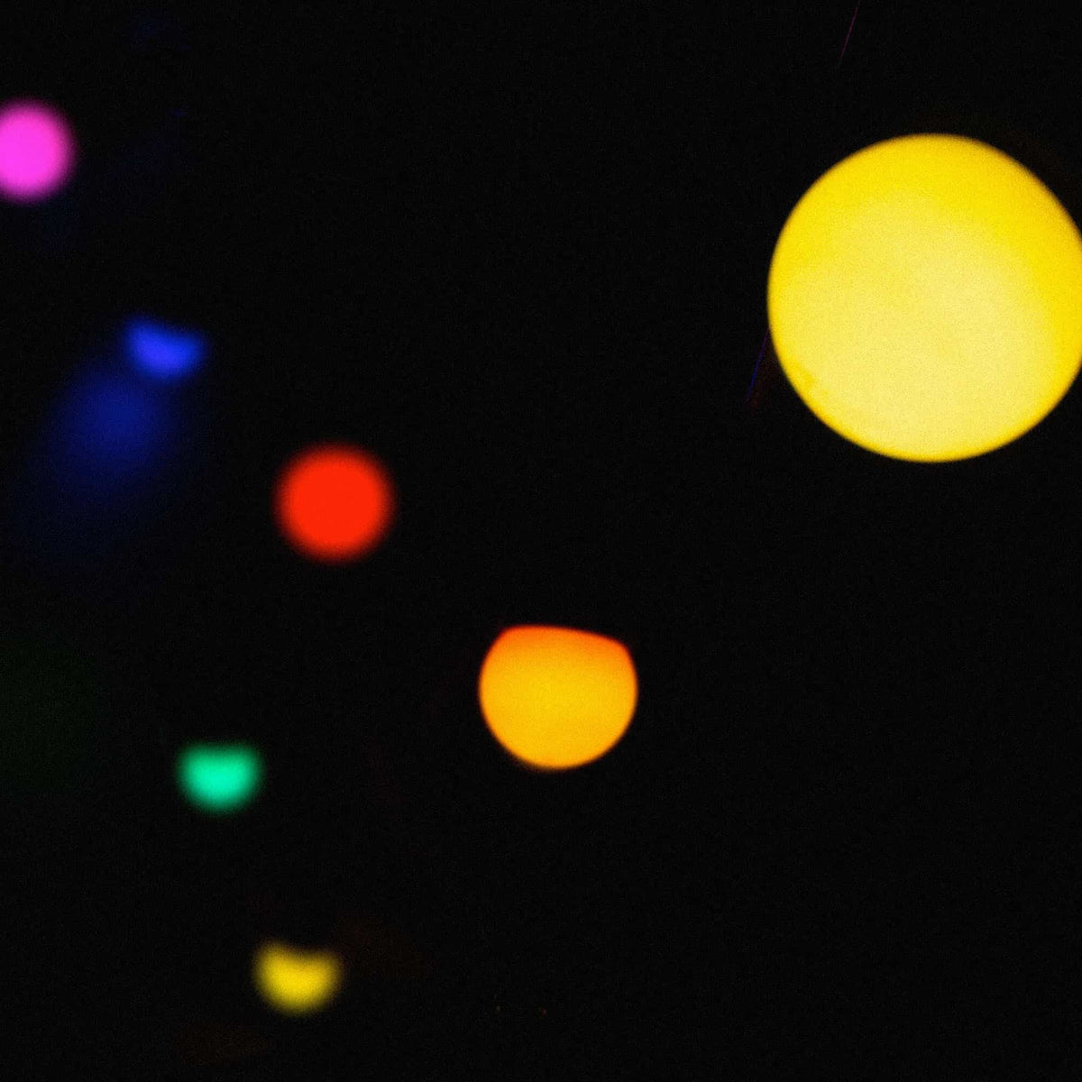 Gros plan d’une guirlande lumineuse multicolore dans l’obscurité, avec plusieurs ampoules floues diffusant des teintes vives de jaune, rouge, vert, bleu et violet.