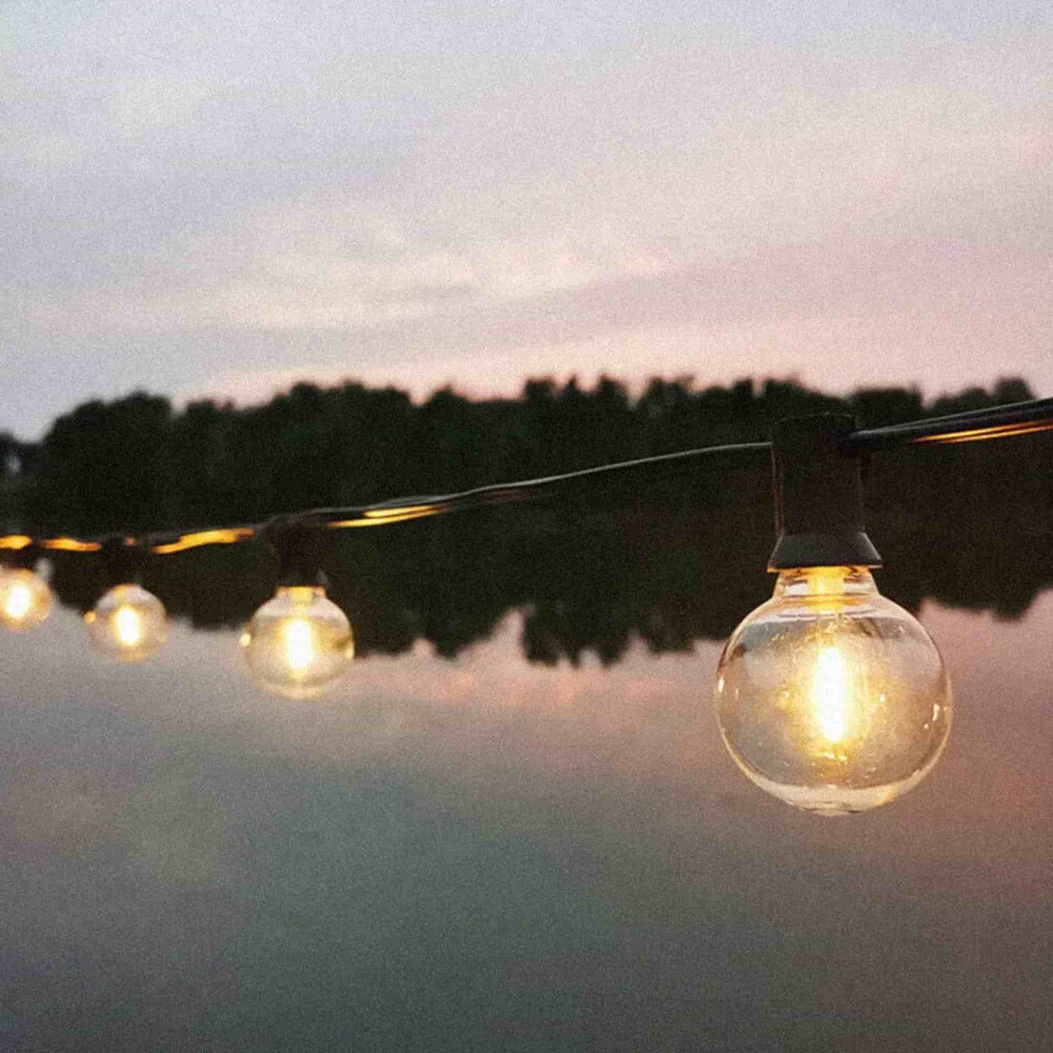 Guirlande lumineuse Goya Forest Grill suspendue au bord de l’eau, diffusant une lumière douce et chaleureuse idéale pour créer une ambiance cosy en extérieur au coucher du soleil.