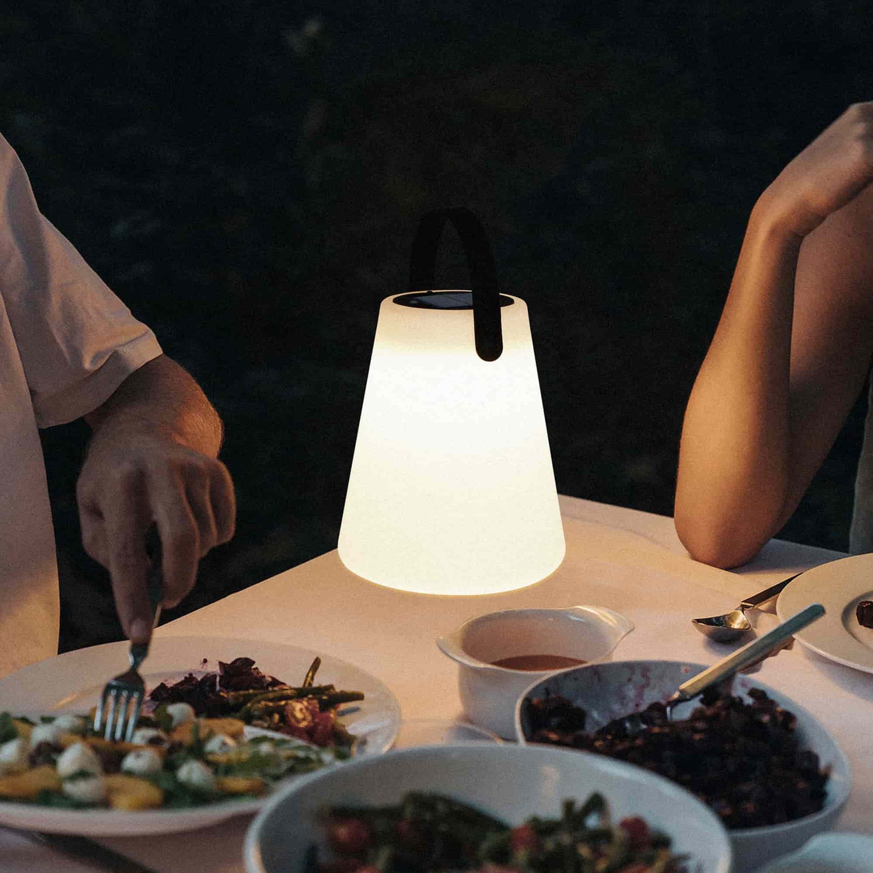 Lampe Cône Forest Grill éclairant une table dressée pour un dîner en extérieur, créant une atmosphère chaleureuse et intime grâce à sa lumière douce et diffuse.