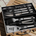 Mallette ouverte sur une table en bois, contenant un ensemble complet d’ustensiles de barbecue en acier inoxydable, rangés avec précision dans des sangles noires.