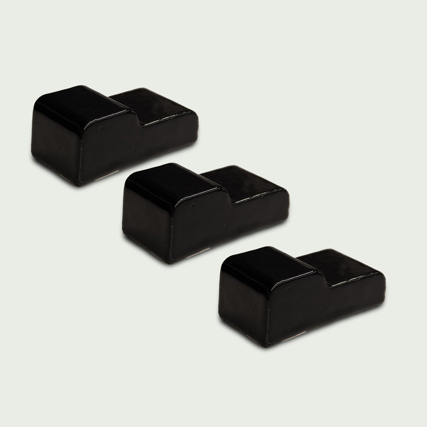 Lot de trois pieds en céramique noirs pour kamado, disposés en diagonale sur fond clair.