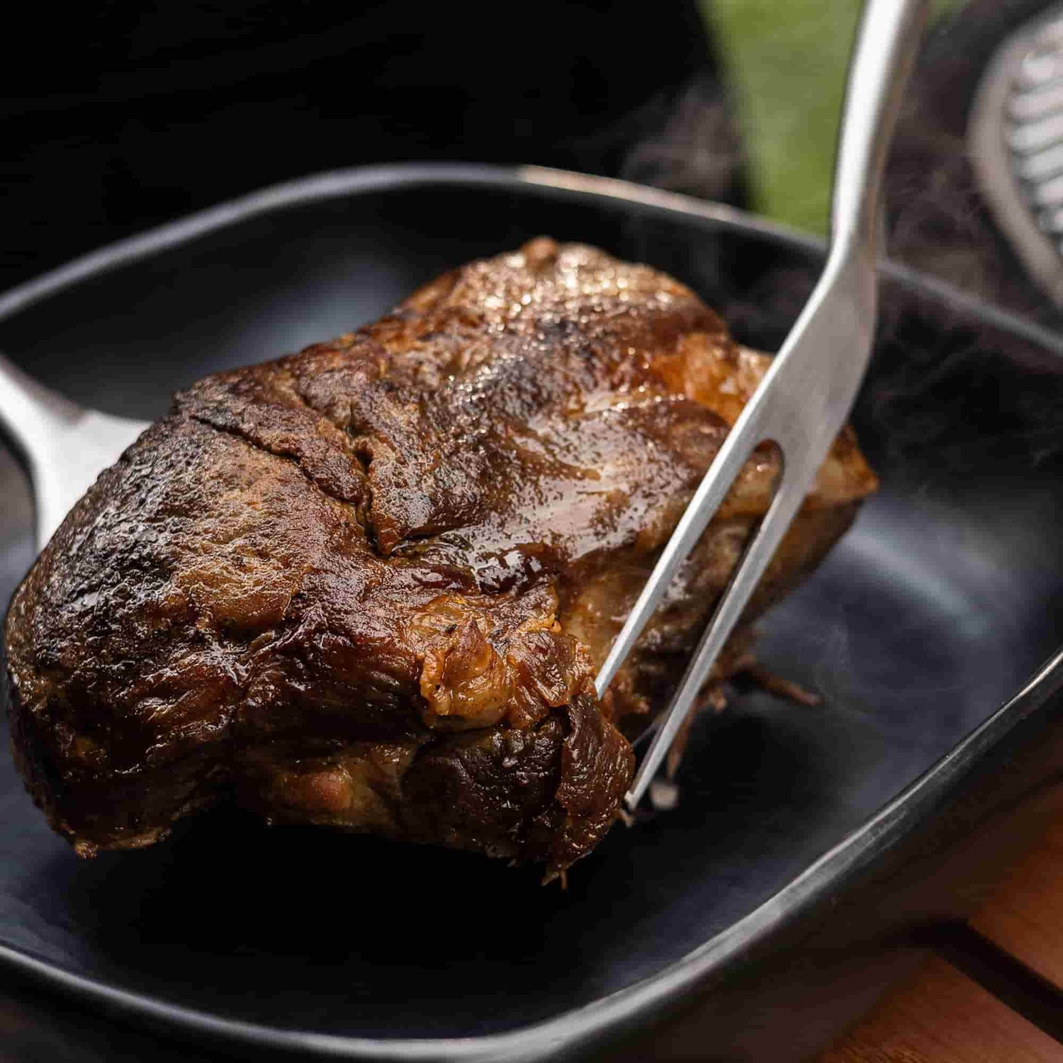 Saftiges Stück gegrilltes Fleisch, gehalten mit einer Grillgabel aus Edelstahl, das noch Dampf abgibt.