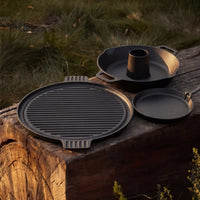 Pack cuisson en fonte Forest Grill avec plancha réversible, poêlon en fonte et support à volaille sur table en bois en extérieur