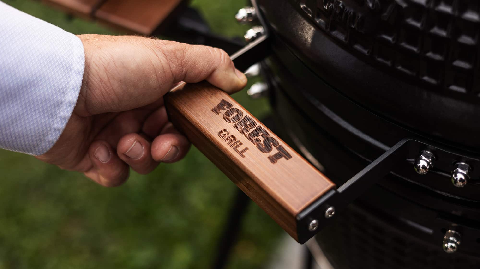 Gros plan sur la poignée en bois gravée Forest Grill d’un barbecue Kamado, symbole de la marque et de son savoir-faire.