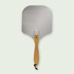 Pelle à pizza en aluminium avec manche court en bois clair et cordelette noire, idéale pour enfourner ou sortir facilement les pizzas du four ou du Kamado.