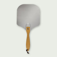 Pelle à pizza en aluminium avec manche court en bois clair et cordelette noire, idéale pour enfourner ou sortir facilement les pizzas du four ou du Kamado.