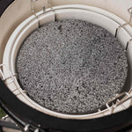 Pierre de lave grise placée dans un support en inox à l’intérieur d’un barbecue Kamado, utilisée pour diffuser la chaleur de manière homogène pendant la cuisson.