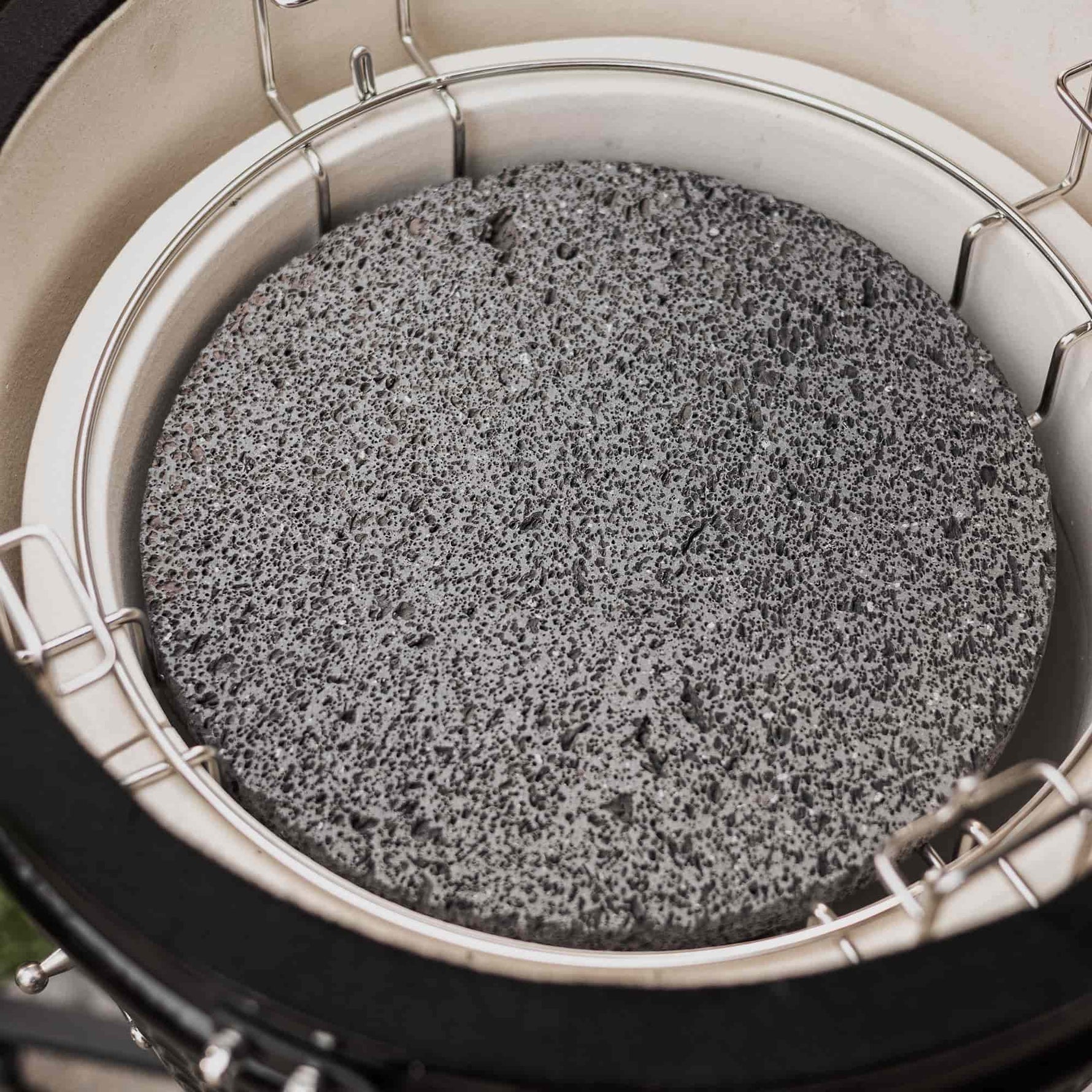 Pierre de lave grise placée dans un support en inox à l’intérieur d’un barbecue Kamado, utilisée pour diffuser la chaleur de manière homogène pendant la cuisson.