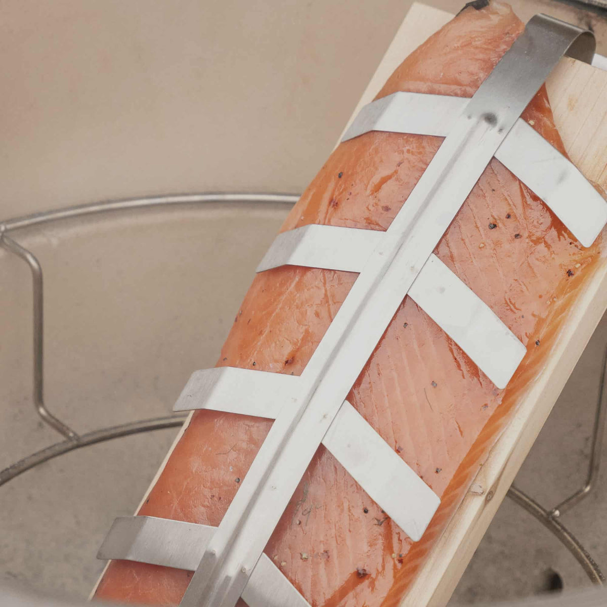 Planche de fumage en bois avec un filet de saumon maintenu par un support inox, prête pour une cuisson lente et aromatique à l’intérieur du barbecue kamado.