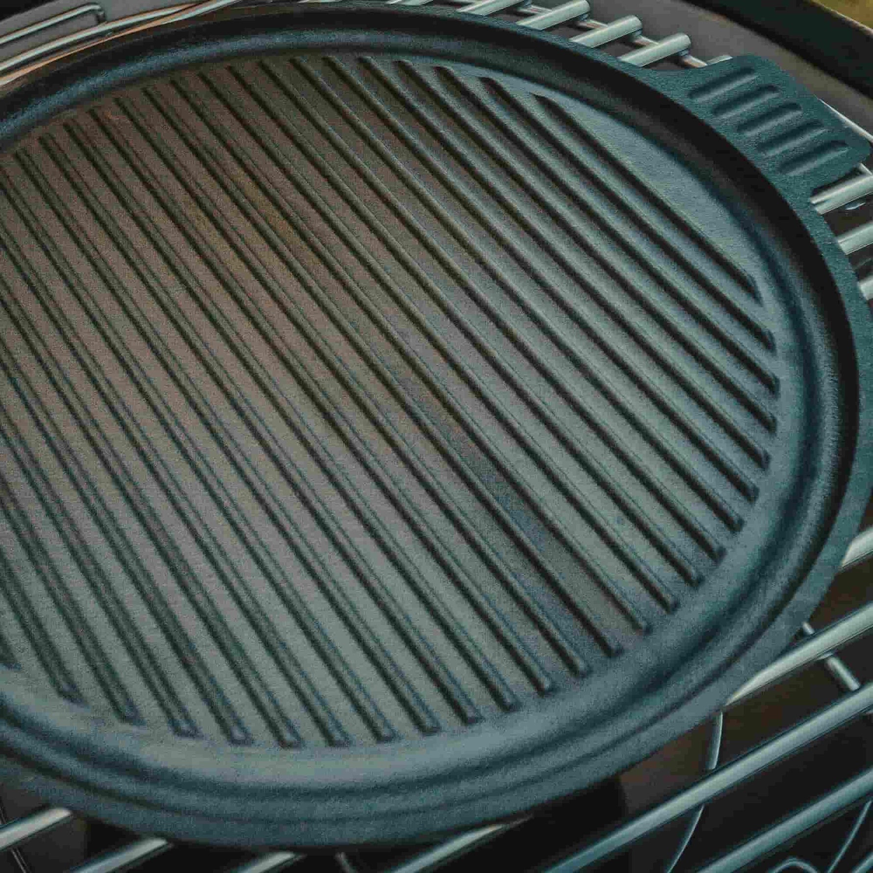Plaque de cuisson en fonte rainurée posée sur la grille du barbecue, parfaite pour marquer les viandes et légumes tout en assurant une cuisson homogène.