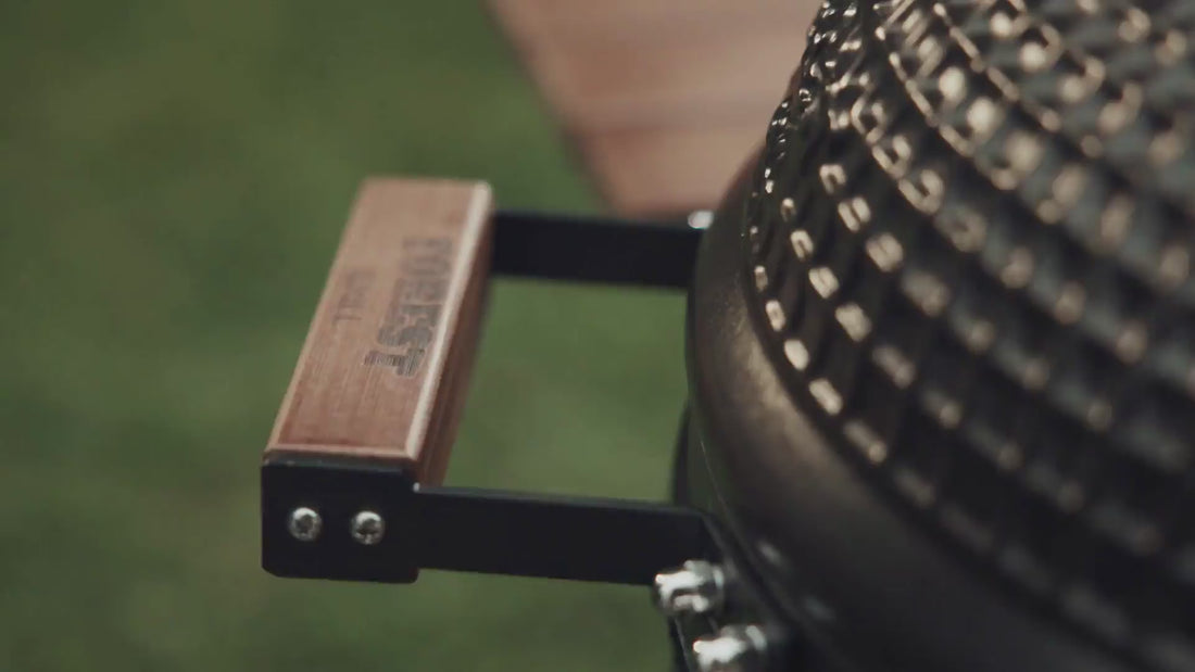 Vidéo montrant le kamado Forest en action, incluant l’ouverture du couvercle, la gestion de la cuisson et l’emploi des différents accessoires. Les détails du kamado — céramique, trappe de fumage, grilles, poignée et roues — sont clairement visibles.