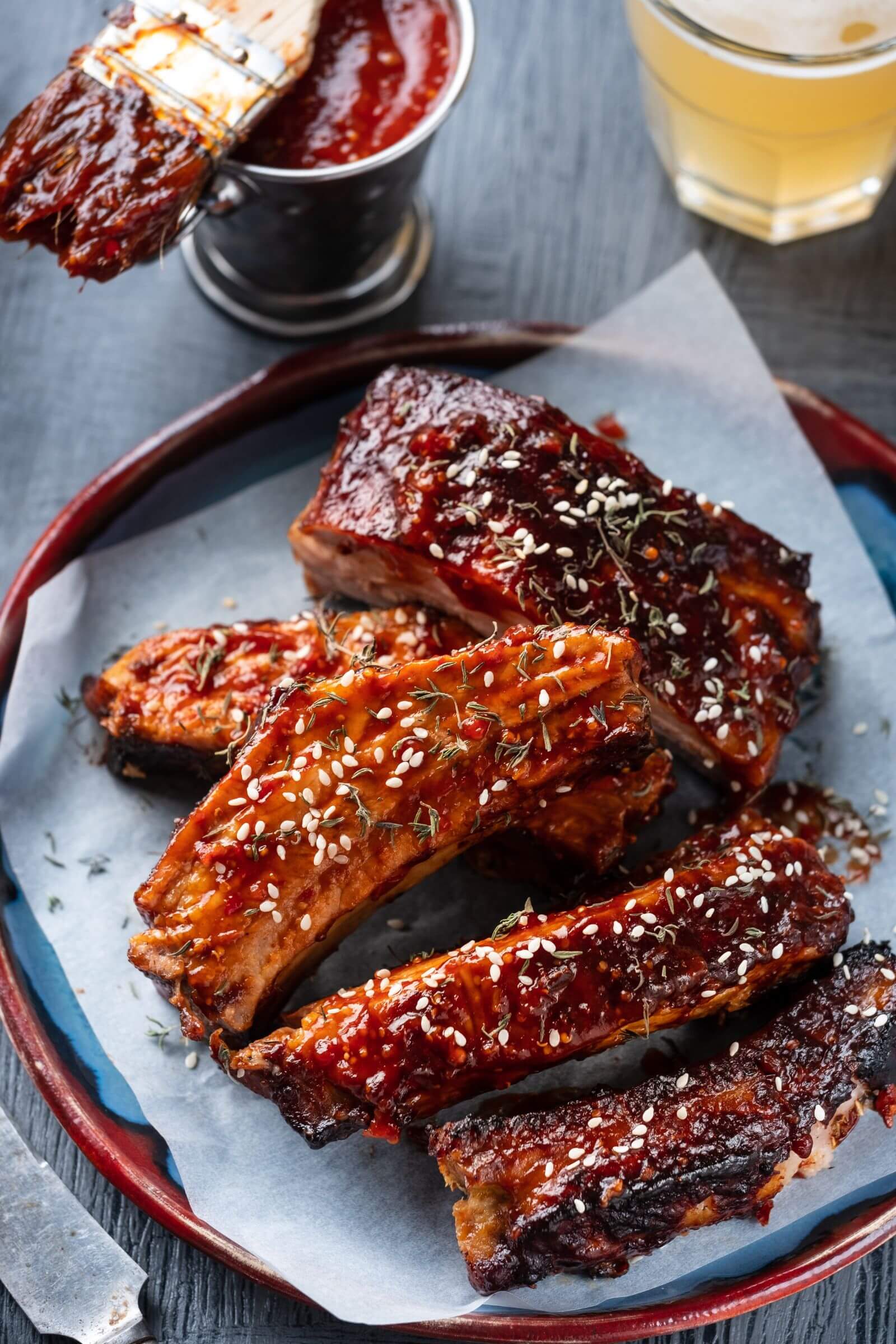 Travers de porc caramélisés nappés de sauce barbecue et parsemés de graines de sésame, servis sur une assiette.