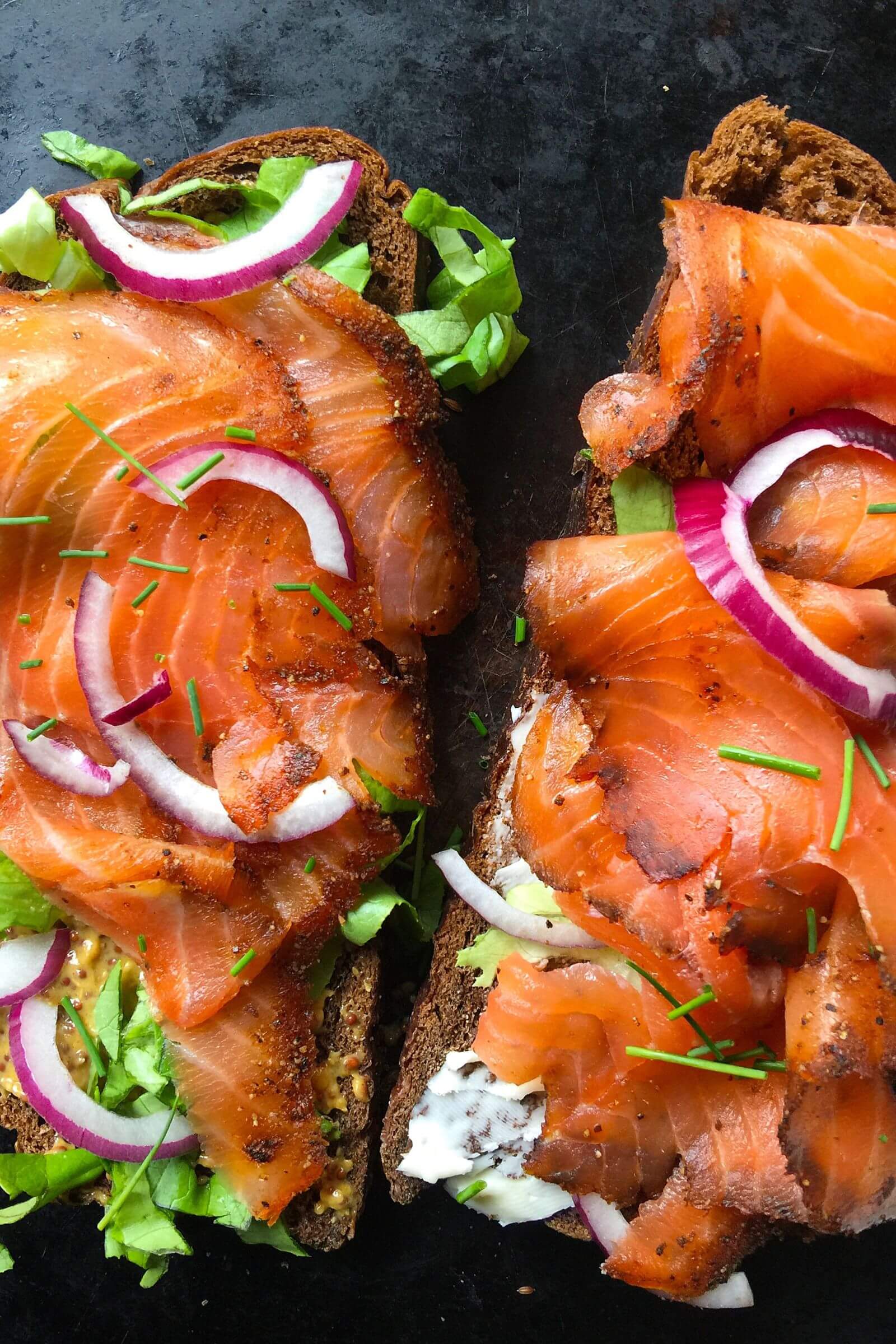 Tartines de pain noir garnies de saumon fumé au kamado, salade verte, oignons rouges et ciboulette fraîche.