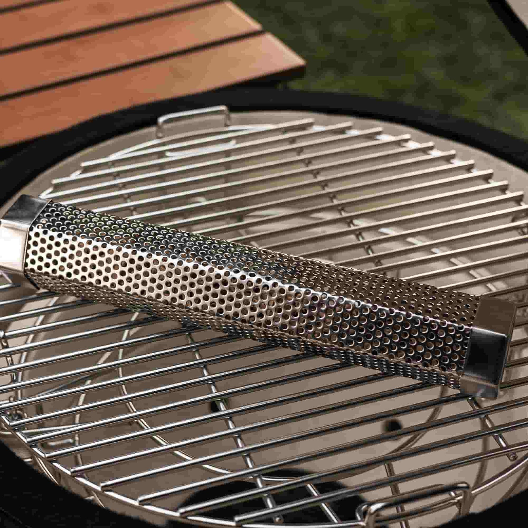 Tube générateur de fumée en acier inoxydable perforé, posé sur la grille d’un barbecue Kamado, prêt à être utilisé pour parfumer les cuissons avec des copeaux de bois.